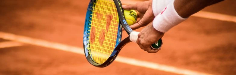 Eine Nahaufnahme der Beine zweier Fußballspieler im Zweikampf um den Ball auf einem Kunstrasenplatz. Ein Spieler in blauer Hose und blauen Stutzen hat seinen linken Fuß am Ball, während der andere Spieler in weißer Hose und weißen Stutzen in einer tiefen, dynamischen Bewegung ebenfalls zum Ball strebt.
